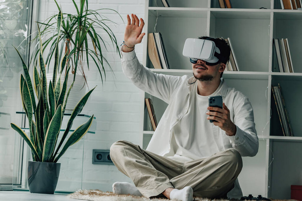 молодий чоловік вдома з окулярами віртуальної реальності та мобільним телефоном - Фото, зображення