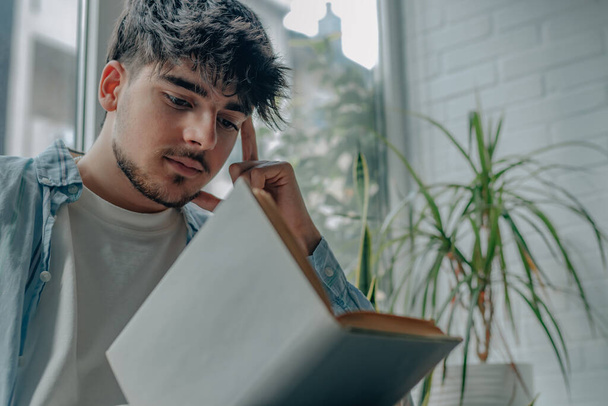 νεαρός άνδρας που διαβάζει ένα βιβλίο ή σπουδάζει στο σπίτι - Φωτογραφία, εικόνα