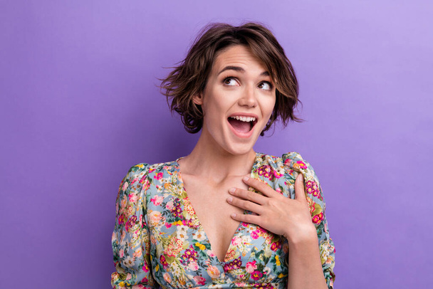 Photo of astonished cheerful pretty lady wear flower print blouse arm breast look up empty space isolated on purple color background. - 写真・画像