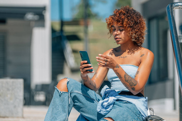 chica latina negra con teléfono móvil en la calle con estilo urbano - Foto, imagen