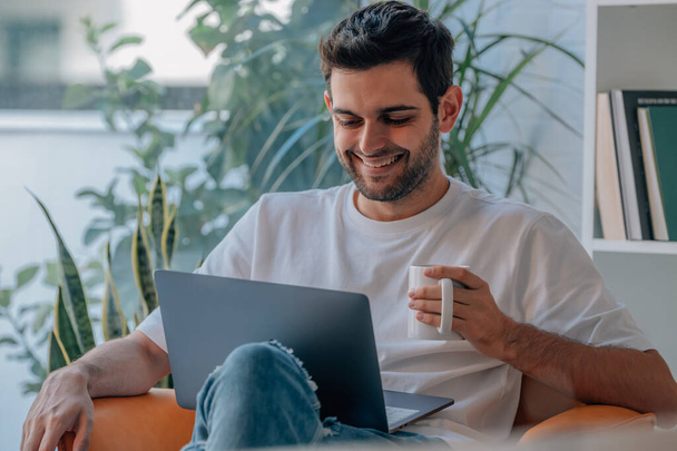 νεαρός άνδρας στο σπίτι με υπολογιστή και φλιτζάνι καφέ - Φωτογραφία, εικόνα