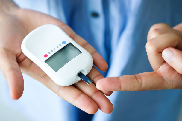 Die Hand der Menschen überprüft Diabetes und hohen Blutzuckerspiegel mit einem digitalen Druckmessgerät. Gesundheitswesen und medizinisches Konzept - Foto, Bild