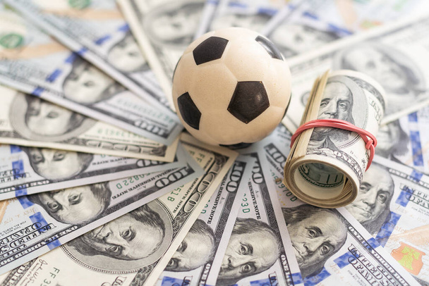 Football little ball lying on a hundred dollar bill. Money and soccer ball - sport and business background. High quality photo - Photo, Image