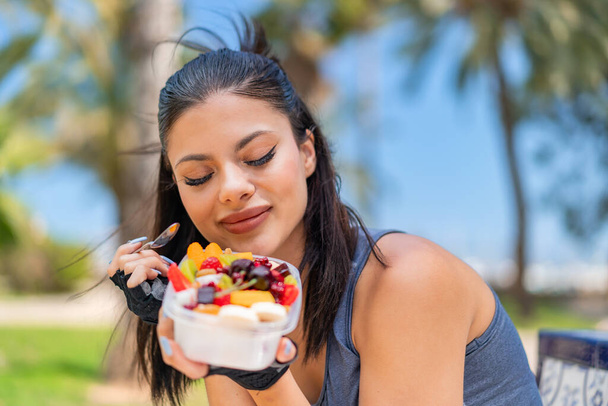 Young pretty sport woman holding a bowl of fruit at outdoors - Photo, Image