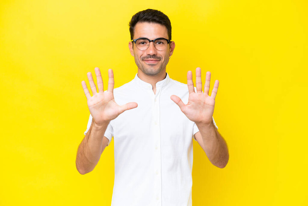 Молодий красивий чоловік над ізольованим жовтим тлом підраховує десять пальцями
 - Фото, зображення
