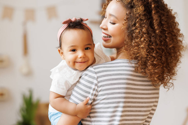 Heureuse et joyeuse mère afro-américaine tient dans ses bras une petite fille qui rit. Concept de maternité et de famille aimante - Photo, image