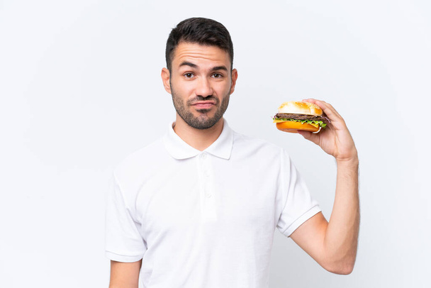 Nuori komea valkoihoinen mies, jolla on hampurilainen syrjäisellä taustalla surullisella ilmeellä - Valokuva, kuva