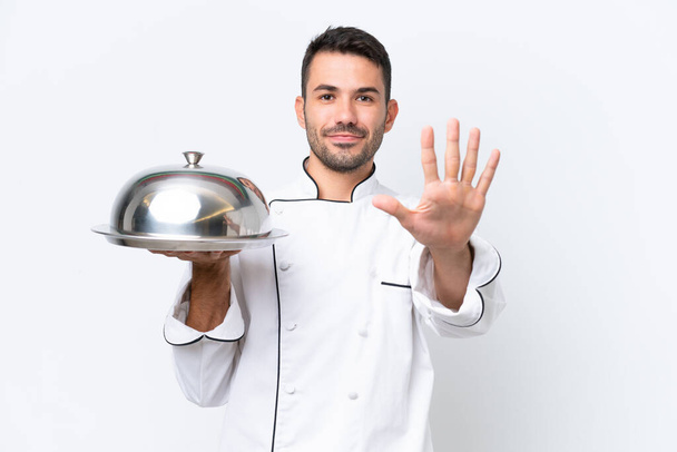 Молодий шеф-кухар з підносом ізольовано на білому тлі підраховуючи п'ять пальцями - Фото, зображення