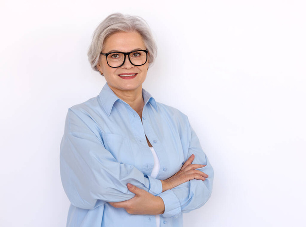 Wesoły dojrzały kobieta przedsiębiorca z siwymi włosami i w okularach stojących ze złożonymi ramionami na białym tle i patrząc w aparat - Zdjęcie, obraz
