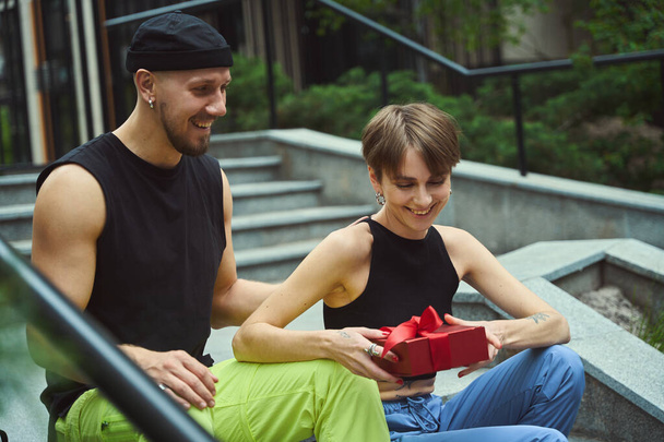Happy woman receiving gift from her boyfriend while sitting on stairs outside - Фото, зображення
