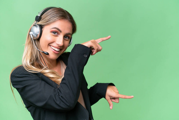 Telemarketer hezká uruguayská žena pracující se sluchátky přes izolované pozadí ukazující prstem na stranu a prezentující produkt - Fotografie, Obrázek