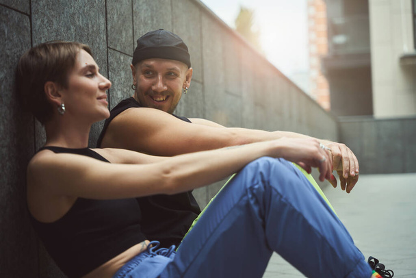 Young informal man and his girlfriend chat while sitting on the sidewalk in a small courtyard in a metropolis - Фото, зображення