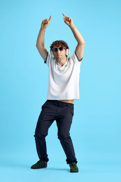 Full-length image of mature man in casual clothes listening to music in headphones and dancing against blue studio background. Concept of human emotions, facial expression, lifestyle - Foto, immagini
