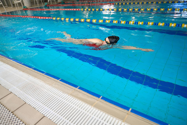 Young female athlete in goggles and swim cap doing front crawl in water - Photo, Image