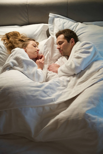 Krásný rodinný pár spí sladce a zdravě, leží v pohodlné ortopedické posteli pod teplou přikrývkou tváří v tvář, odpočívá v noci - Fotografie, Obrázek