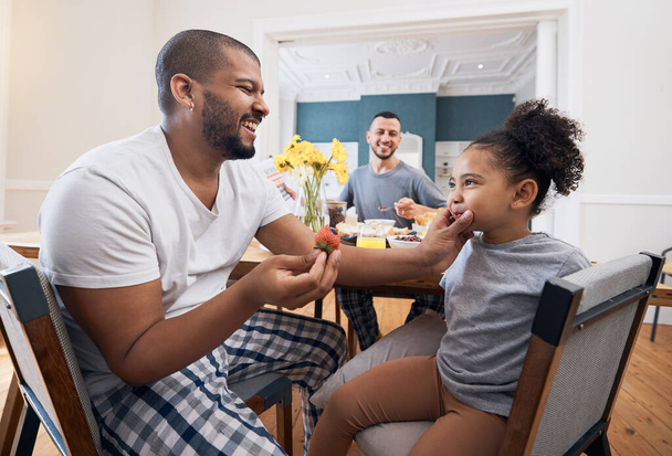 Gay couple, breakfast or child with father wipe, cleaning or remove food, morning meal or cereal from mouth of girl. Happy family, adoption or non binary dad smile for hungry youth kid eating at home. - Photo, Image