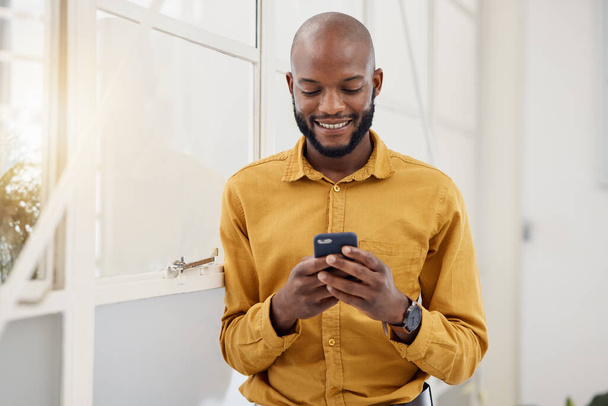 Business, happy black man and typing with phone in office for social network, mobile website and internet contact. Employee scroll on smartphone chat, reading news app and notification of information. - Photo, image