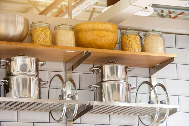 Ollas y tapas con frascos para almacenamiento de alimentos en los estantes de la cocina - Foto, Imagen
