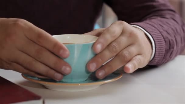 ソーサーからコーヒーと一緒にカップを取る男性の手の近く. 男はソーサーの端に手を置きました. ソーサーに青いコップを戻す男 - 映像、動画