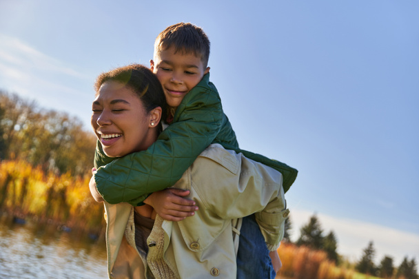 Familienliebe, fröhlicher afrikanisch-amerikanischer Junge umarmt Mutter, herbstliche Natur, geschlossene Augen, Glück - Foto, Bild