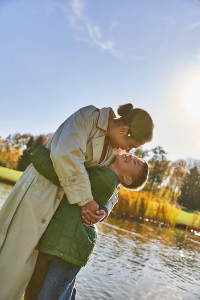 vínculo familiar, amor, madre afroamericana feliz y el niño abrazando cerca del lago, la naturaleza, el otoño, sonrisa - Foto, Imagen