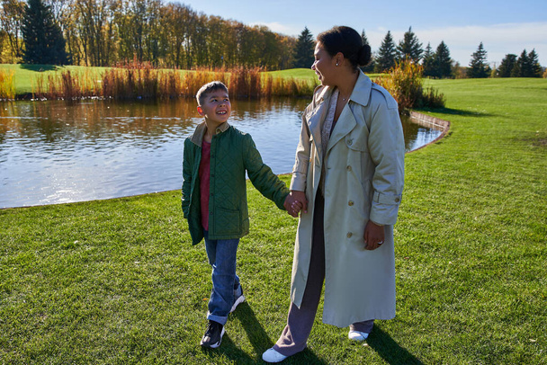 bonding, happy mother and son holding hands and walking near lake in park, african american family - Fotografie, Obrázek