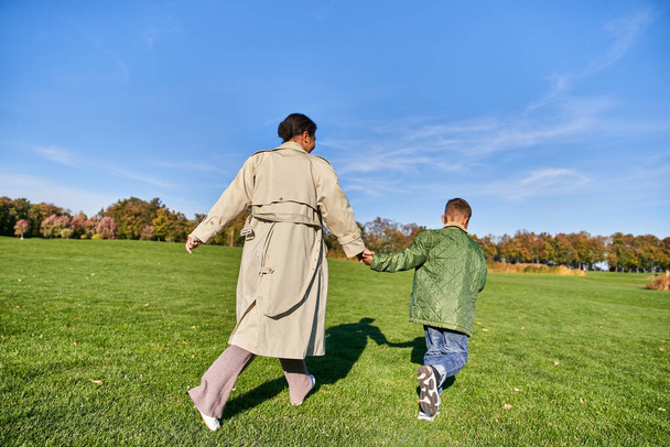 játékos, afro-amerikai nő fut együtt fia a parkban, őszinte, napos nap ősszel - Fotó, kép