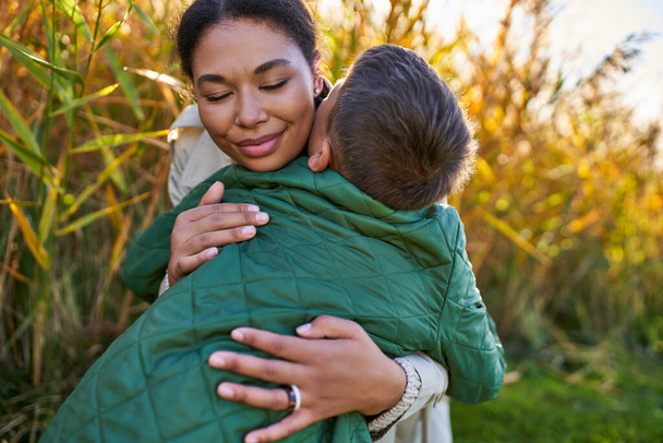 bonheur, amour maternel, mère afro-américaine étreignant son fils en vêtements d'extérieur automnaux, saison d'automne - Photo, image
