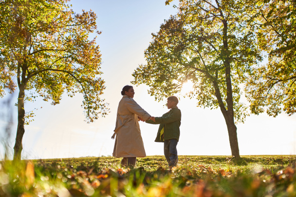 silueta de la madre y el niño tomados de la mano en el parque de otoño, temporada de otoño, vinculación y amor - Foto, Imagen