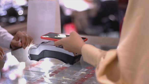 Mobilna azjatycka muzułmanka korzystająca z telefonu komórkowego - smartwatch płacący za produkt w terminalu sprzedaży z płatnością identyfikacyjną nfc za weryfikację i uwierzytelnianie - Zdjęcie, obraz