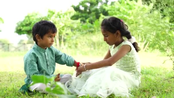 Мила індійська дівчина в сукні зв'язує браслет для свого маленького брата на руці - Кадри, відео
