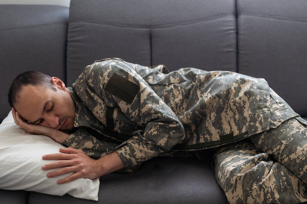 blurred boy looking at exhausted dad in camouflage sleeping on couch in living room with christmas decoration. High quality photo - Photo, Image