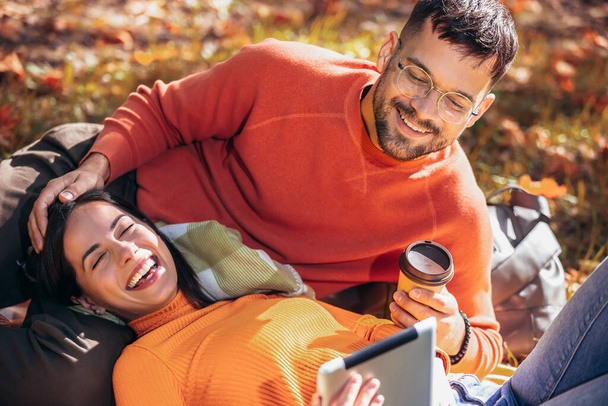 Młoda para patrząca na tabliczkę podczas picia kawy. Słoneczny jesienny dzień w kolorowym parku - Zdjęcie, obraz
