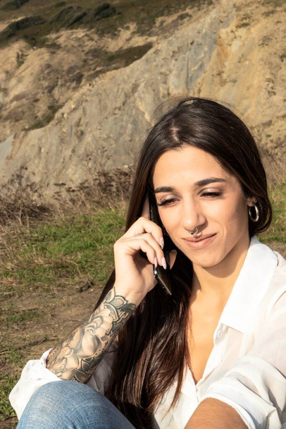 Morena de confianza con el brazo del tatuaje habla por teléfono, irradiando vibraciones casuales Chic - Foto, Imagen