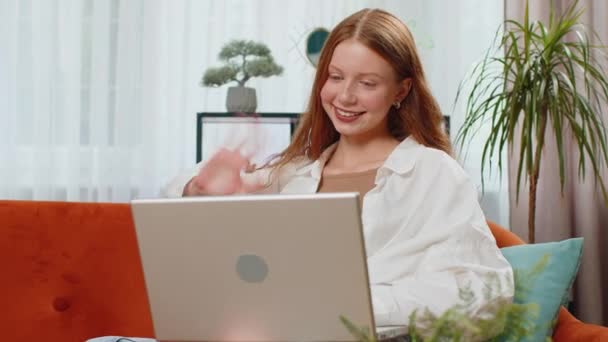 Teenager κόκκινο κορίτσι μαλλιά κάνοντας βιντεοκάμερα κλήση συνέδριο με φίλους ή την οικογένεια, απολαμβάνοντας ευχάριστη συνομιλία. Παιδί χρήση φορητού υπολογιστή για να μιλήσει με το δάσκαλο, μελέτη, εκπαίδευση στο σπίτι κάθεται στον καναπέ του δωματίου - Πλάνα, βίντεο