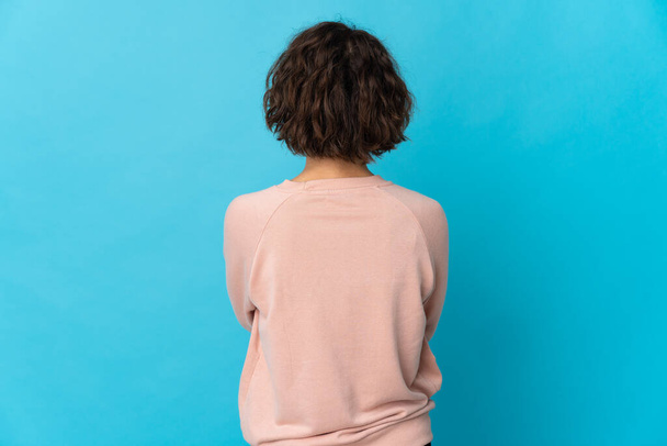 Young English woman isolated on blue background in back position - Valokuva, kuva