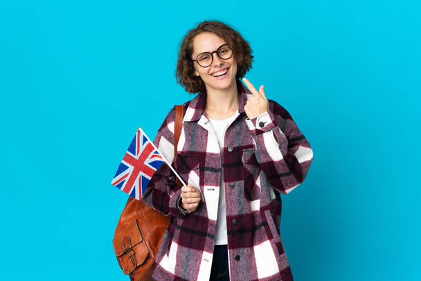 Young English woman holding an United Kingdom flag isolated on blue background giving a thumbs up gesture - Photo, Image