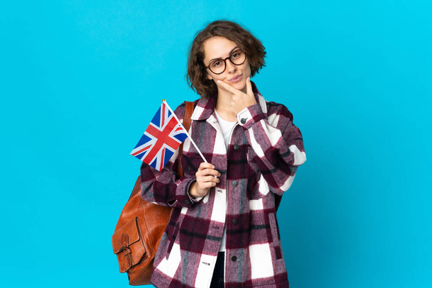 Young English woman holding an United Kingdom flag isolated on blue background thinking - Foto, imagen