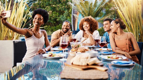 Селфі, група друзів за обідом в саду і вечірці за столом з різноманітністю, їжею і вином разом. Фотографії, чоловіки і жінки за обіднім столом, щасливі люди їдять з напоями на задньому дворі - Фото, зображення