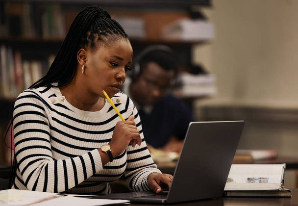 Diák, nő és gondolkodás laptopon a könyvtárban tanulásra, kutatásra és egyetemi ötletekre vagy fókuszra. Fiatal afrikai személy számítógépen olvasási és e-tanulási célok, oktatás vagy online tervezés. - Fotó, kép
