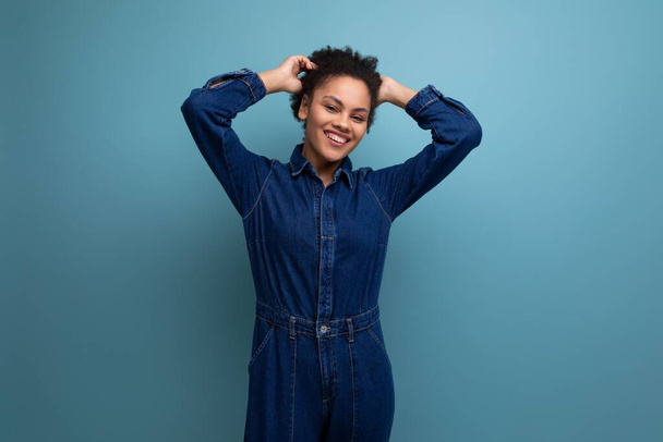 young well-groomed hispanic business woman with fluffy hair dressed in blue denim overalls isolated with copy space background. - Photo, Image
