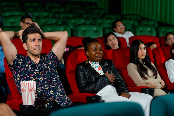 Grupo de personas multiéticas se sientan en asientos en el cine y se ven aterradores o terifican durante la película. - Foto, imagen