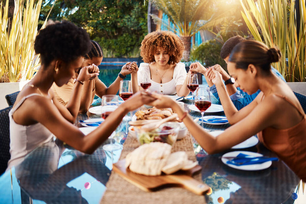 People, food and holding hands to pray outdoor at table for gratitude and holiday celebration. Group of people together at lunch, party or reunion with drinks in garden for thanks, prayer and grace. - Photo, Image