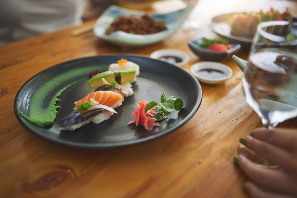 Bord, tafel en sushi met een persoon in een restaurant voor vis, lunch of zeevruchten diner. Close-up, honger en mensen in een café voor lekker eten, Chinees eten of het eten van Aziatische gerechten voor een maaltijd samen. - Foto, afbeelding