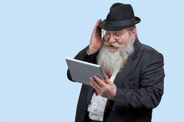 Uśmiechnięty starszy pan czyta wiadomości na tablecie cyfrowym. radosny podekscytowany Dojrzałe mężczyzna za pomocą przenośny komputer odizolowany na niebieski. - Zdjęcie, obraz
