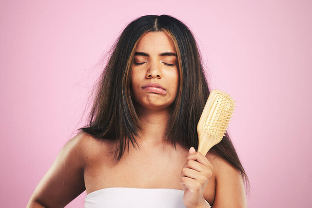 Hair care, frustrated and woman with brush ready for salon beauty treatment in a studio. Brushing, upset and Brazilian hairstyle growth with female model from Brazil with problem and pink background. - Photo, Image