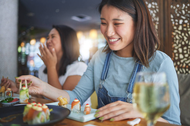 Γιαπωνέζα γυναίκα, εστιατόριο και να τρώει σούσι με χαμόγελο, ξυλάκια και ενθουσιασμένος για καλό φαγητό στο πάρτι. Ασιάτες φίλοι, ψάρια και υγιεινά με τον πολιτισμό, παραδοσιακά ή fast food σε εστιατόριο, μπαρ ή κατάστημα. - Φωτογραφία, εικόνα