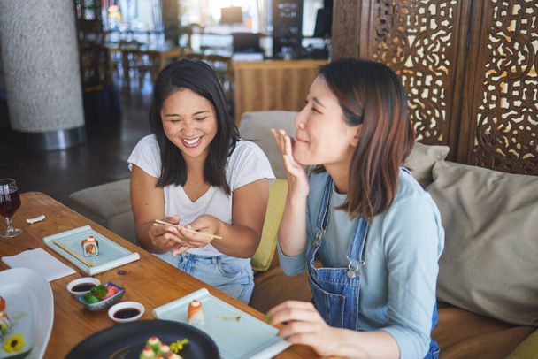 Girl friends, sushi restaurant and eating together with comic laugh, joke and fail with chopsticks at table. Japanese women, happy and excited with fish, seafood or diner with help, mistake or memory. - Photo, Image