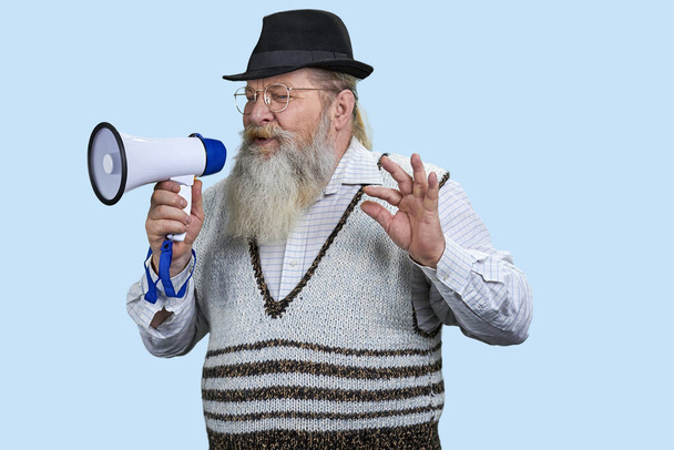 Portret starszego brodatego mężczyzny przemawiającego w megafonie. Izolacja na pastelowym niebieskim tle. - Zdjęcie, obraz