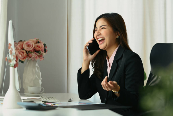 Feliz mujer de negocios asiática hablando por teléfono móvil y riendo, expresando emociones positivas. - Foto, Imagen